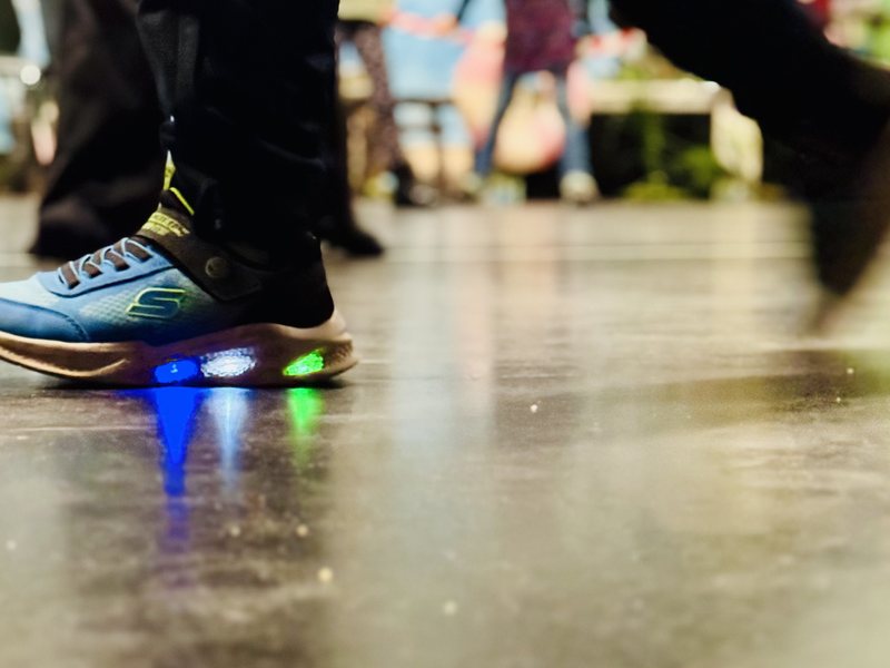 Kinderschuhe mit leuchtenden Sohlen in Bewegung auf dem Hallenboden, der Rest des Raums unscharf